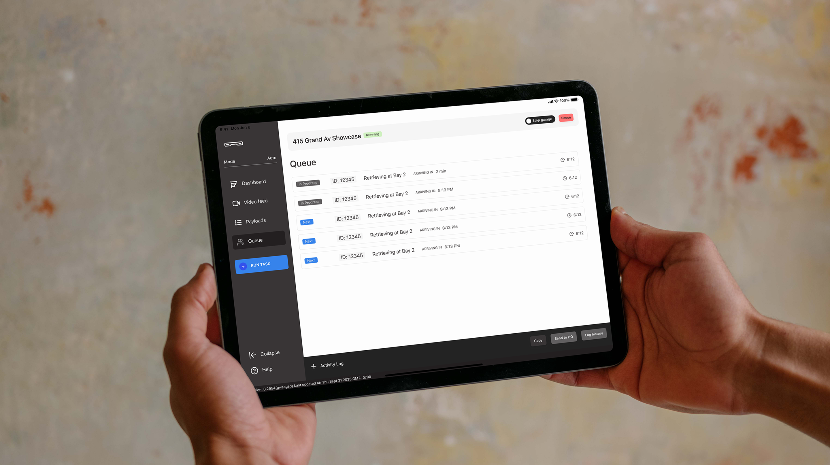 Attendant holding tablet showing the queue view for 415 Grand Av Showcase with vehicle bays listed